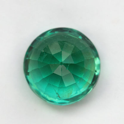 Reverse view of the round green emerald on white, showing pavilion facets meeting at the center.
