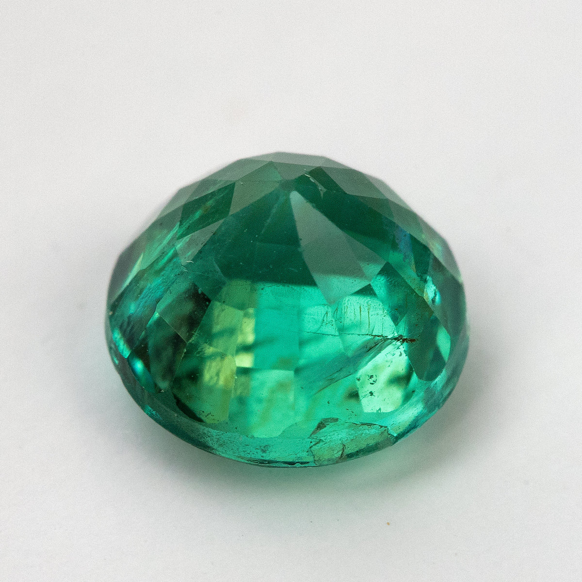 Side profile of the round green emerald on white, showing crown, girdle, and pavilion depth.