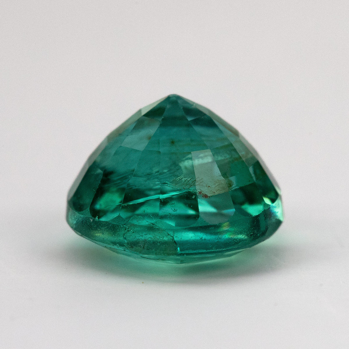 Second side profile of the round green emerald on white from a lower angle.