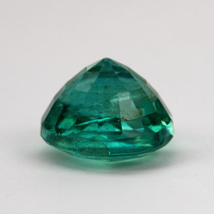 Second side profile of the round green emerald on white from a lower angle.