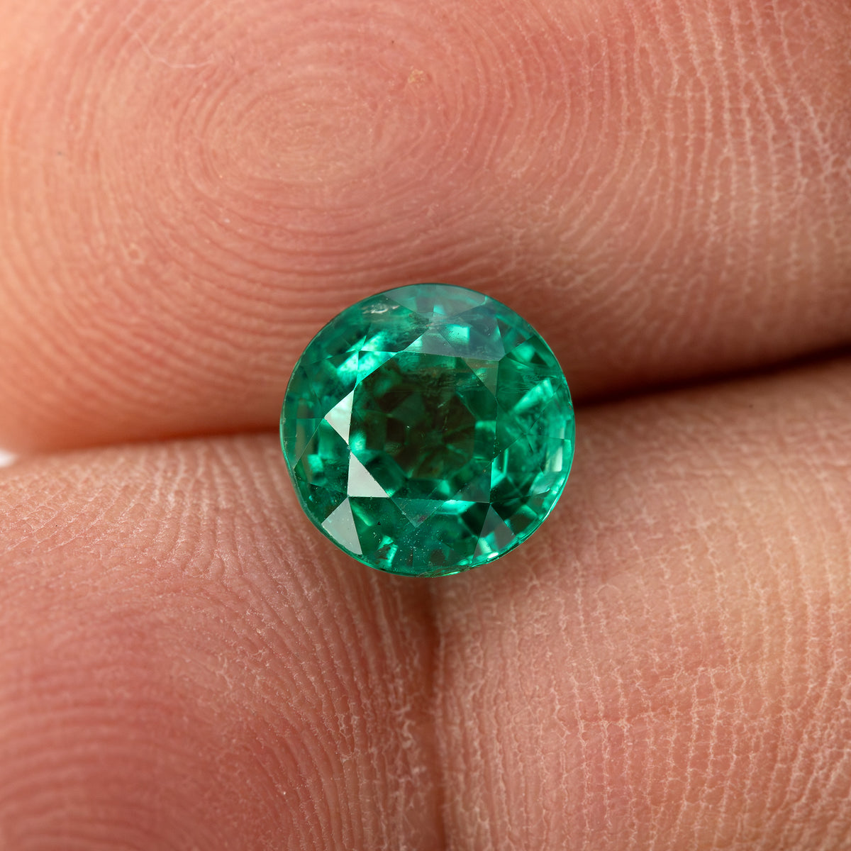 Round green emerald resting face-up on a fingertip for relative scale.