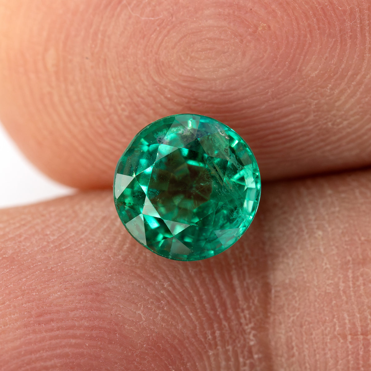 Fingertip view of the round green emerald with a pale central reflection and full circular outline.