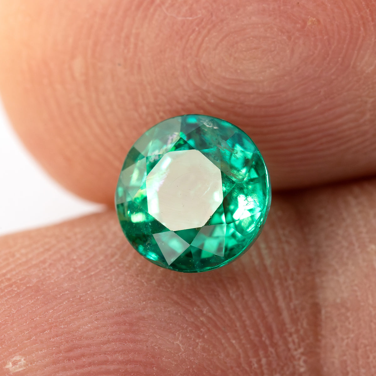 Reverse fingertip view of the round green emerald, showing the pavilion facet pattern.