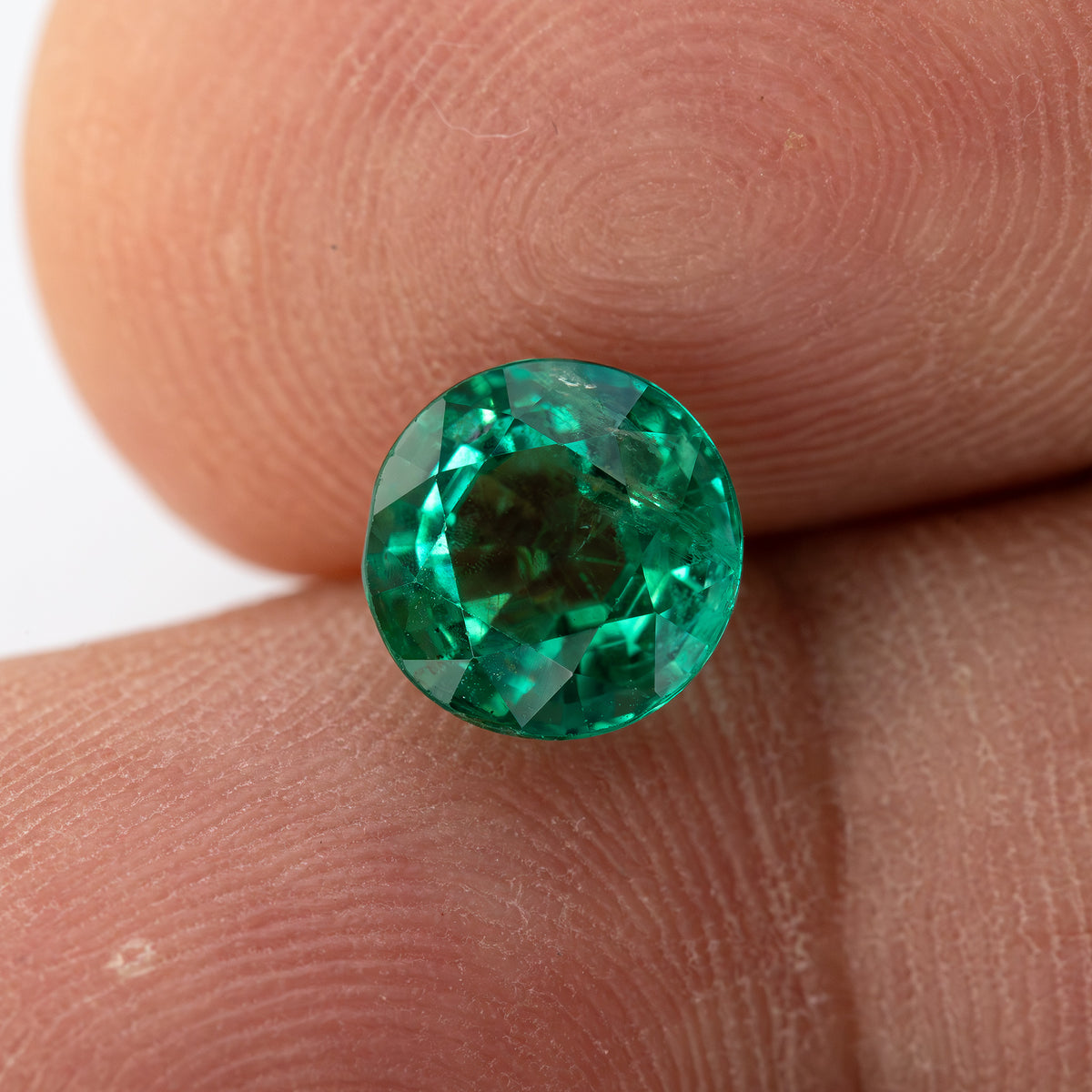 Alternate fingertip view of the round green emerald with a darker center and bright rim facets.