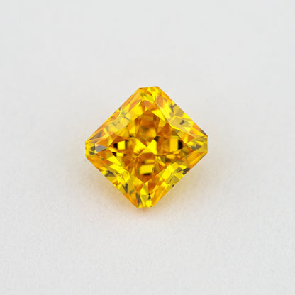 Face-up orange-yellow diamond on a pale surface, showing its cut-cornered rectangular outline and bright crown facets.