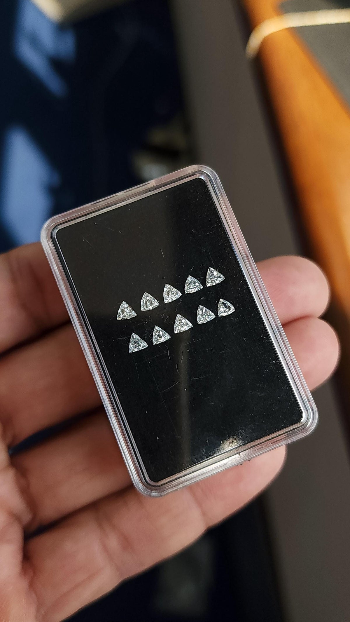 Ten loose trillion-cut diamonds on a black pad in a clear case held at an angle across a hand. Representative stock.