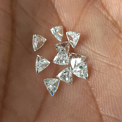 Several loose trillion-cut diamonds scattered in a palm, showing their triangular outlines and different viewing angles. Representative stock.