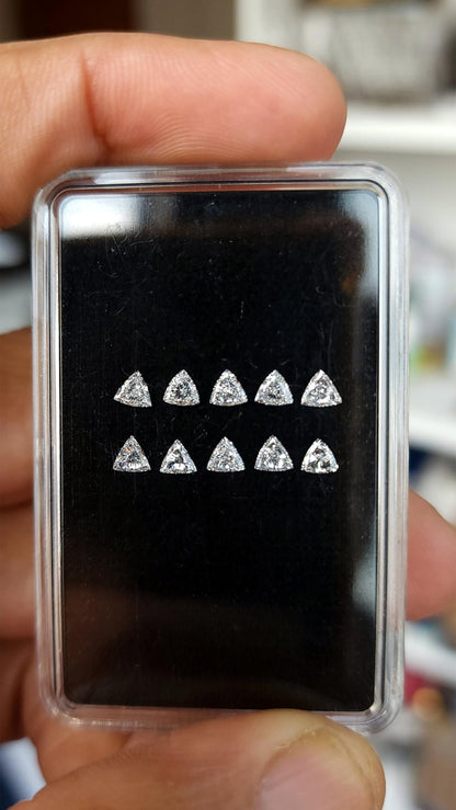 Ten loose trillion-cut diamonds arranged in two rows inside a clear case with a black pad, held between fingers. Representative stock.