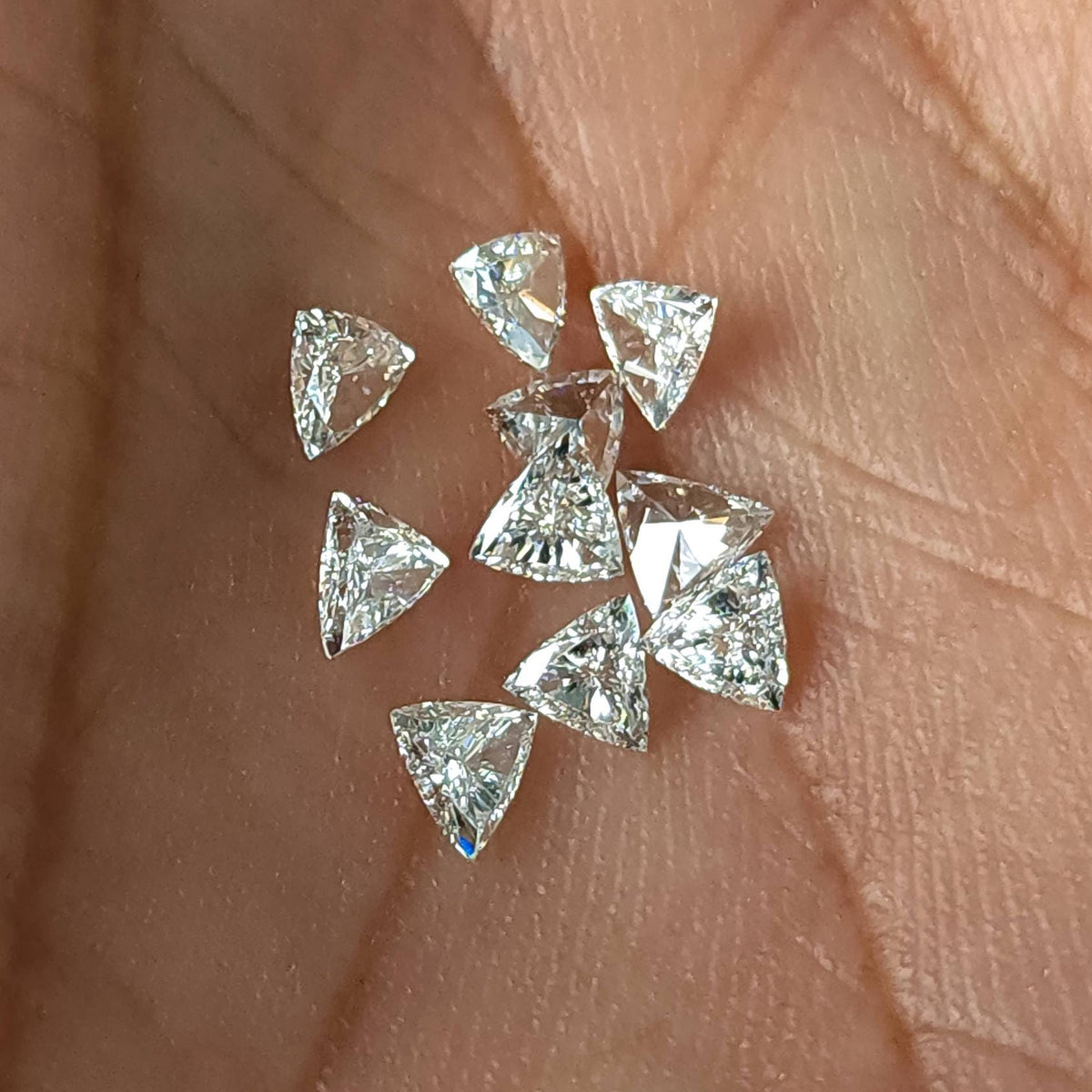 Several loose trillion-cut diamonds scattered in a palm, showing their triangular outlines and different viewing angles. Representative stock.