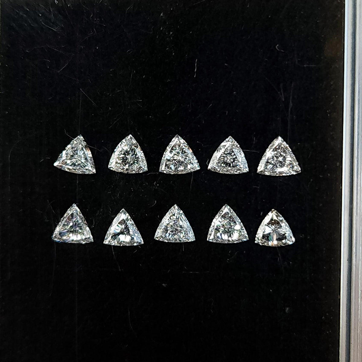 Ten loose trillion-cut diamonds in two rows on a black display pad, showing differences in their reflections. Representative stock.