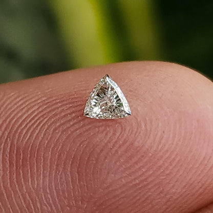 A loose trillion-cut diamond resting face-up on a fingertip, with fingerprint ridges visible for scale. Representative stock.