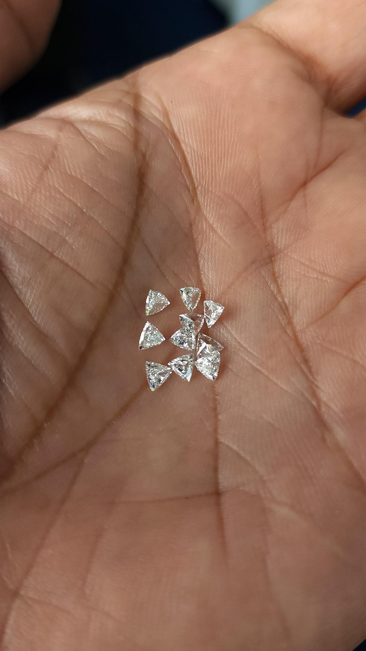 A small group of loose trillion-cut diamonds resting in an open palm, with palm lines visible for scale. Representative stock.