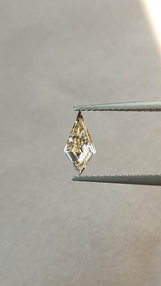 Light champagne lab-grown diamond in an elongated kite step cut held upright in tweezers, showing the exact stone face-up.
