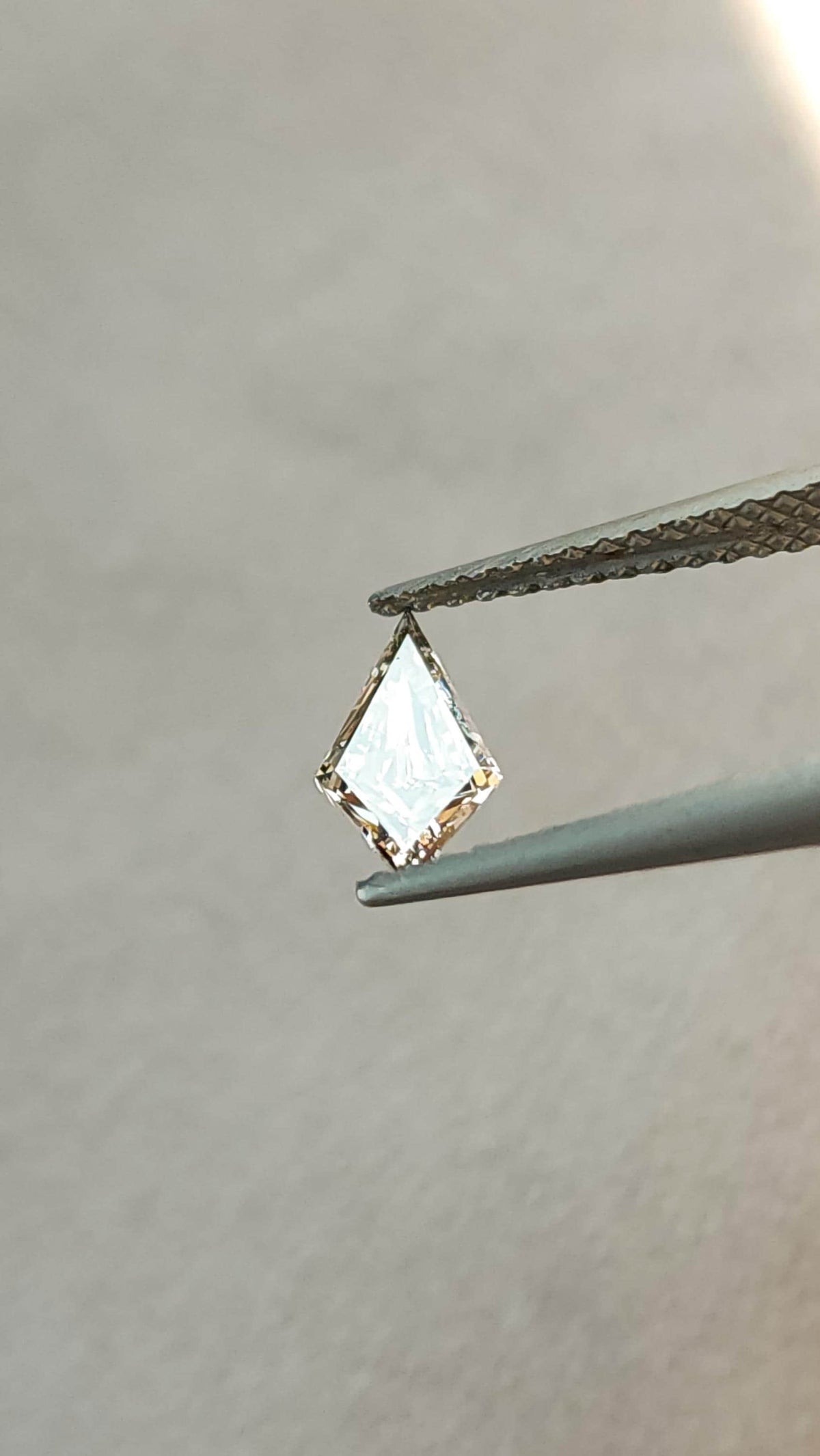 Exact 0.39-carat elongated kite lab-grown diamond held in tweezers at a reflective angle, showing a bright face-up view.