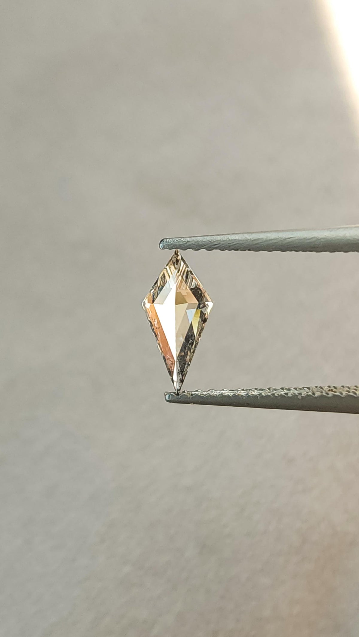 Tilted view of the exact elongated kite lab-grown diamond in tweezers, showing its pointed outline and geometric facets.