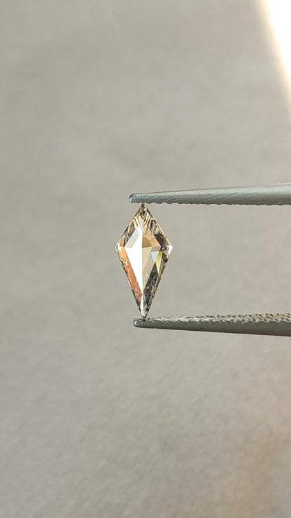 Tilted view of the exact elongated kite lab-grown diamond in tweezers, showing its pointed outline and geometric facets.