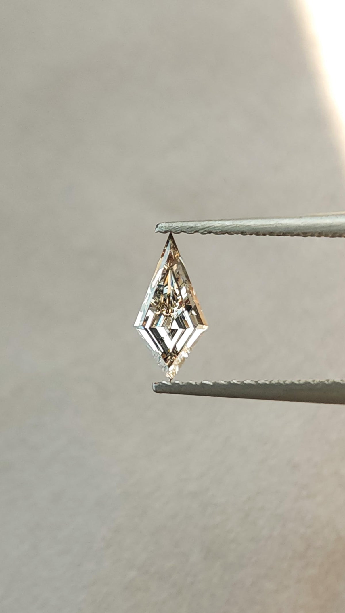 Face-up view of the exact light champagne elongated kite lab-grown diamond in tweezers, showing geometric step-cut reflections.