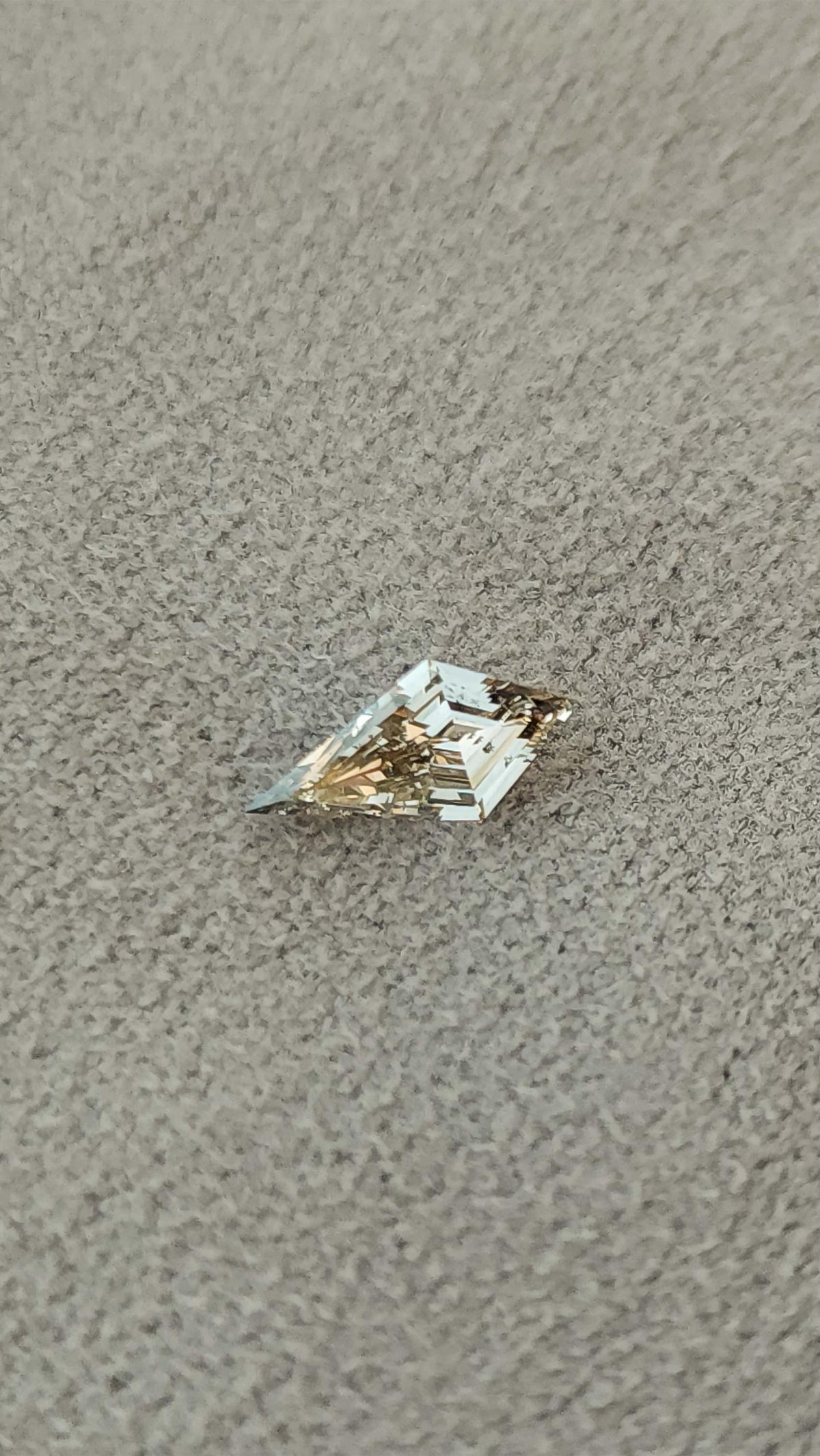 Exact light champagne elongated kite lab-grown diamond resting diagonally on a textured beige surface.