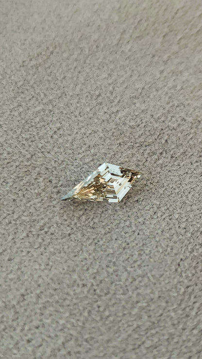 Exact light champagne elongated kite lab-grown diamond resting diagonally on a textured beige surface.