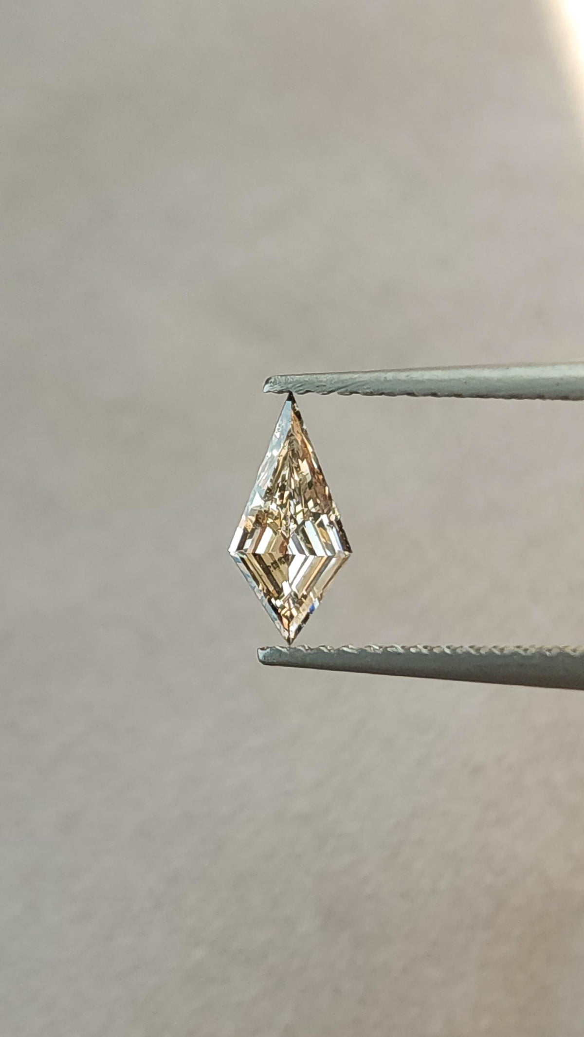Alternate face-up view of the exact light champagne elongated kite step-cut diamond held upright in tweezers.