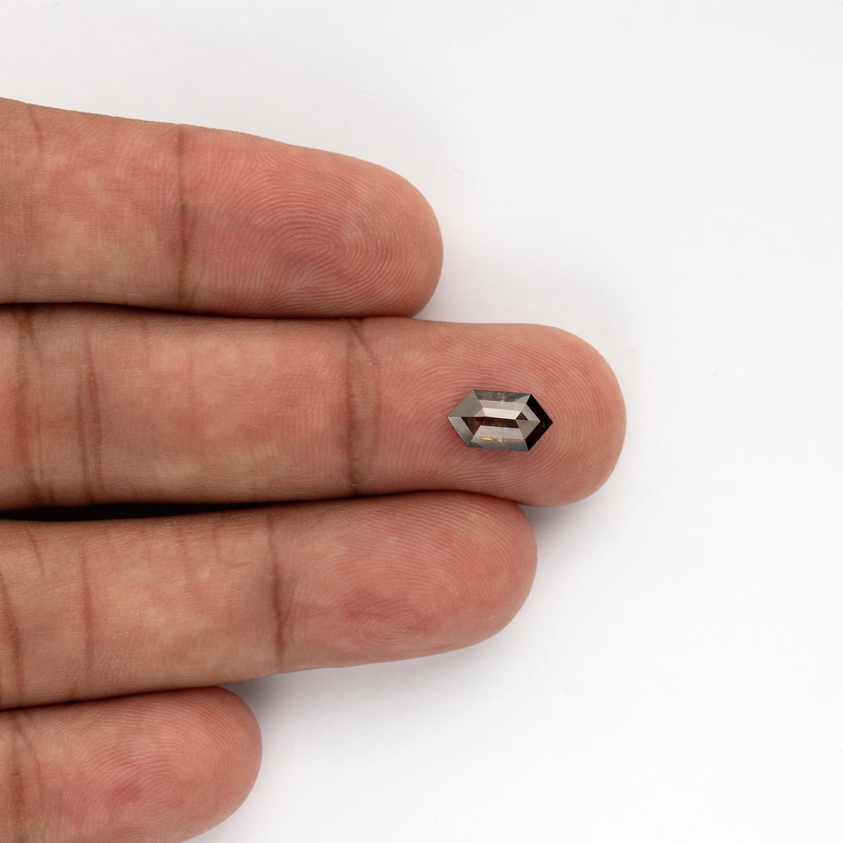 Exact 1.15 ct dark brown Dutch marquise diamond on fingertips, showing its elongated hexagonal outline and scale.