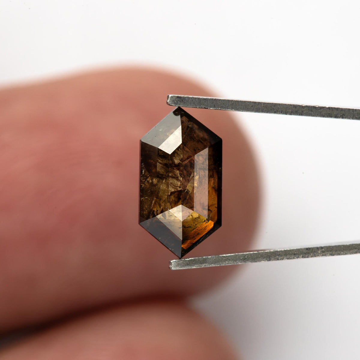 Elongated hexagon diamond held upright above a fingertip, showing its pointed ends, brown reflections and scale.