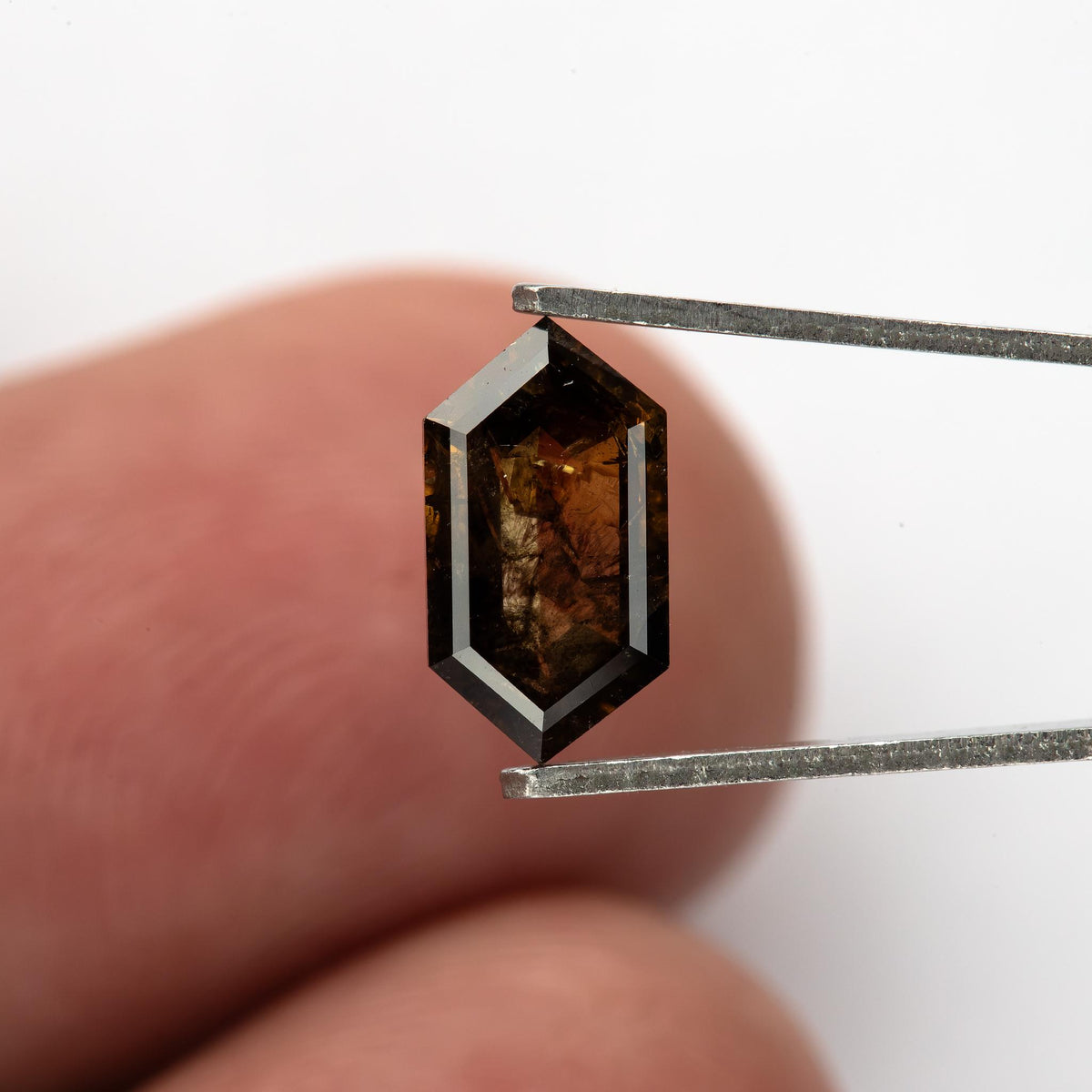 Exact 1.15 ct brown diamond held face-up above a fingertip, showing its elongated proportions and scale.