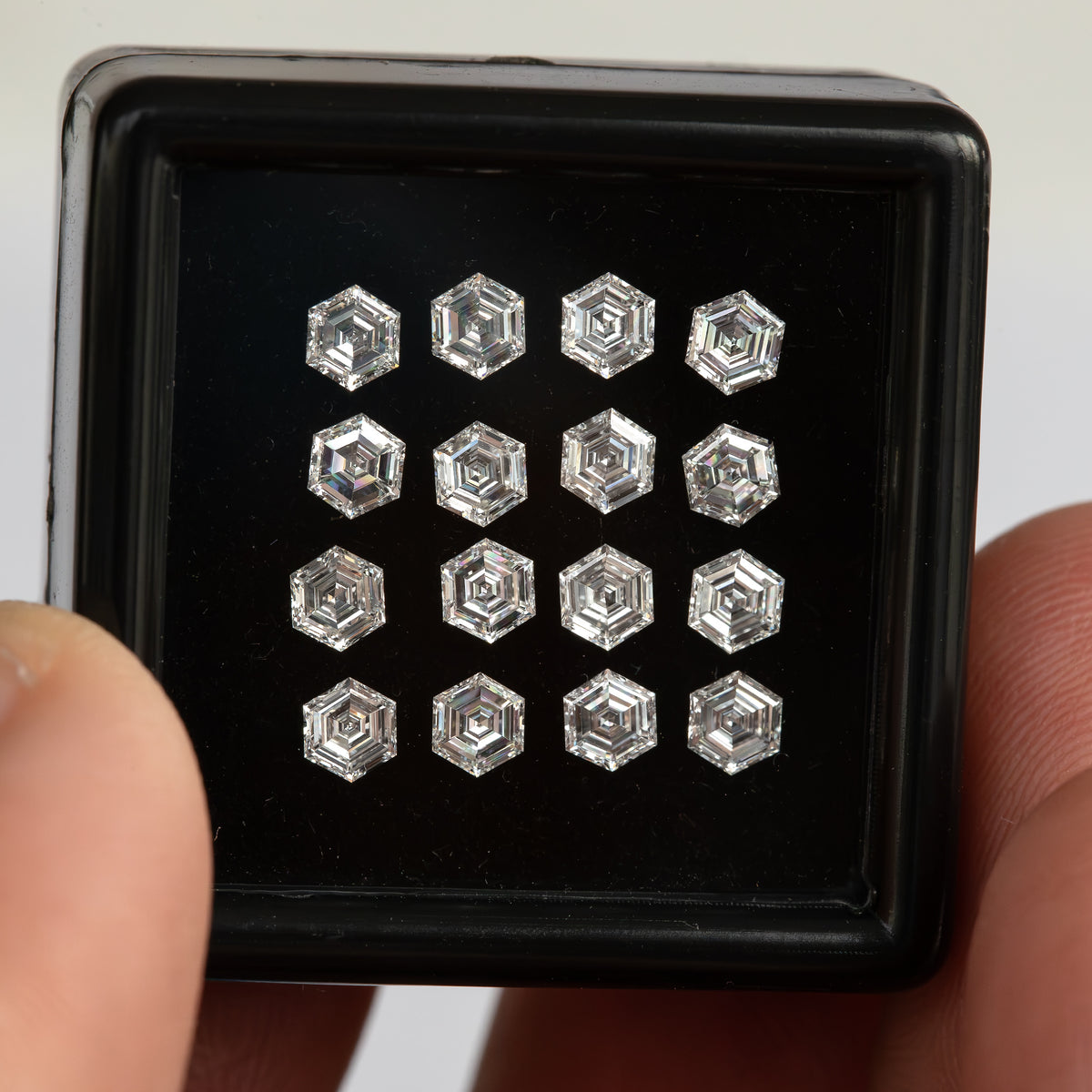 Hexagonal step-cut diamonds arranged face-up in a black tray held between fingers, with pale reflections along the facets.