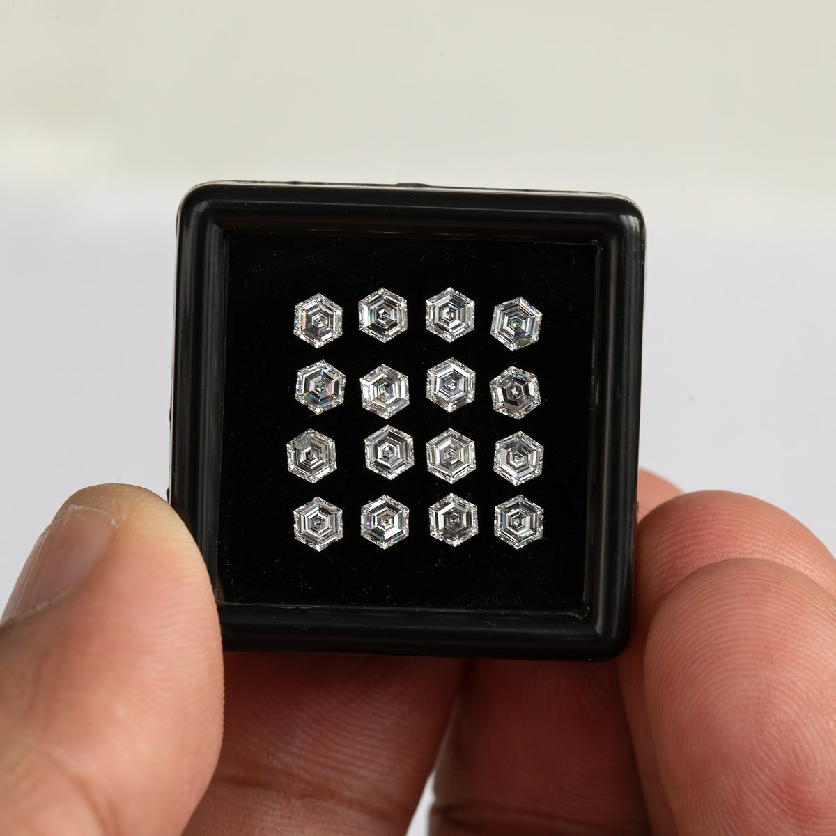 Black diamond tray held between fingers at arm's length, showing the small size of the arranged hexagonal stones.