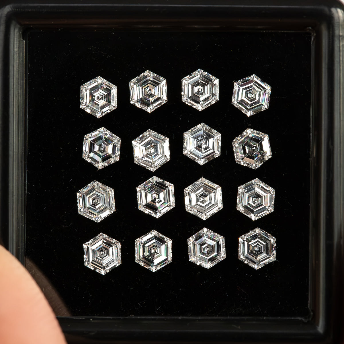 Close view of face-up hexagonal diamonds in a black tray, with concentric step reflections visible across the arrangement.