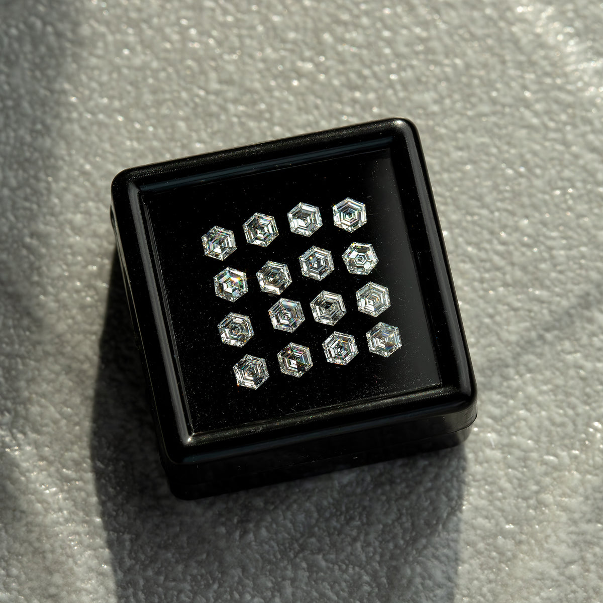 Angled black tray resting on a gray textured surface, showing a face-up group of hexagonal diamonds.