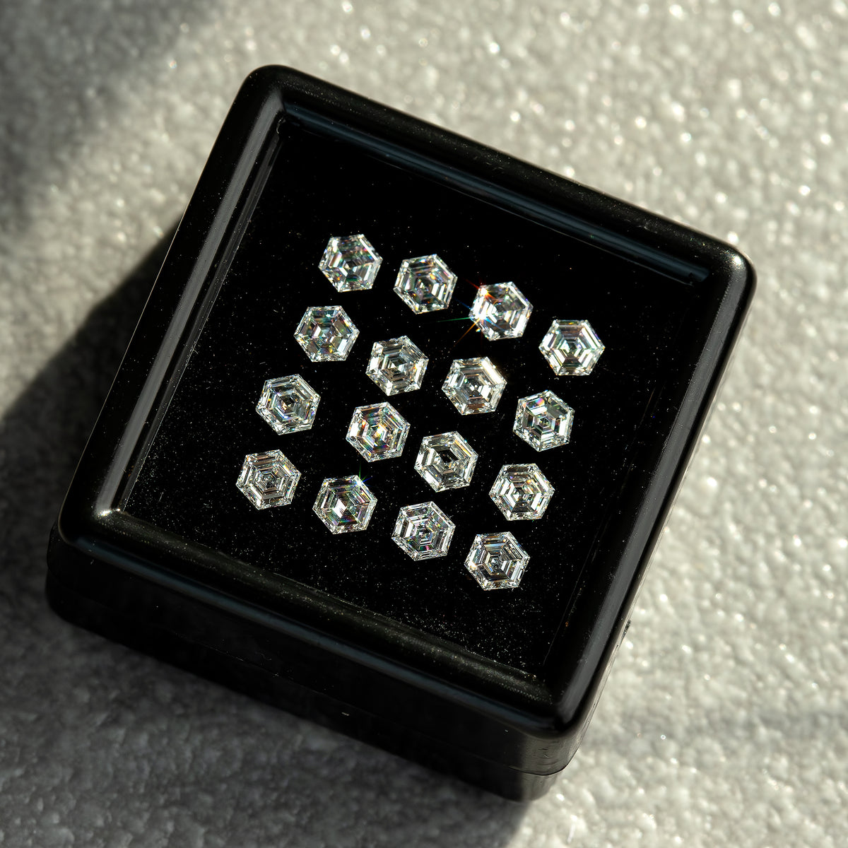 Diagonal tray view of hexagonal diamonds against black backing, with different bright facet reflections.
