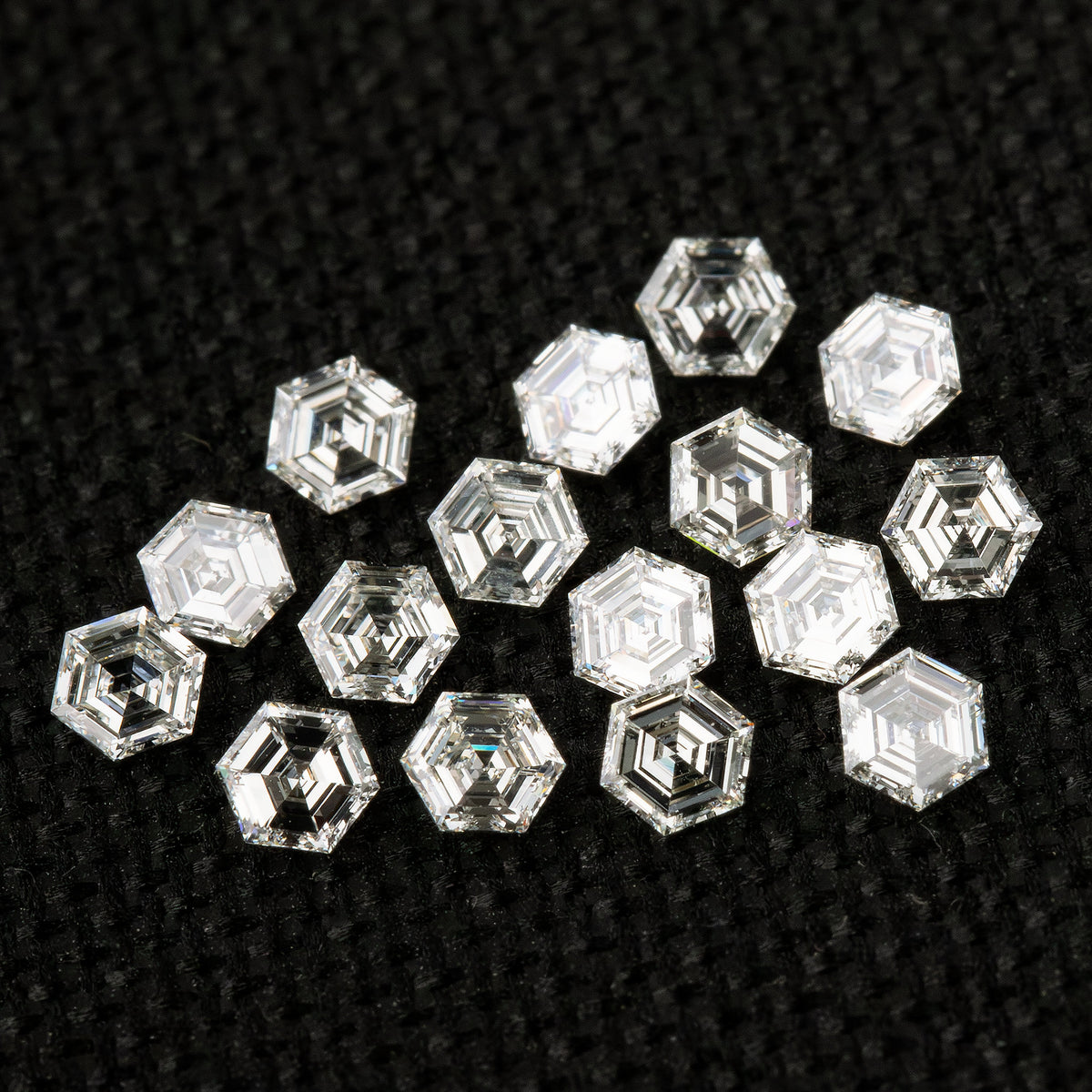 Loose hexagonal diamonds on black fabric in mixed orientations, showing both step-facet faces and differently reflecting reverse views.