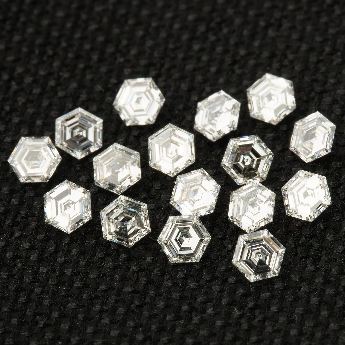 Group of loose hexagonal diamonds on black fabric at an alternate angle, with mixed faces and reflective undersides.