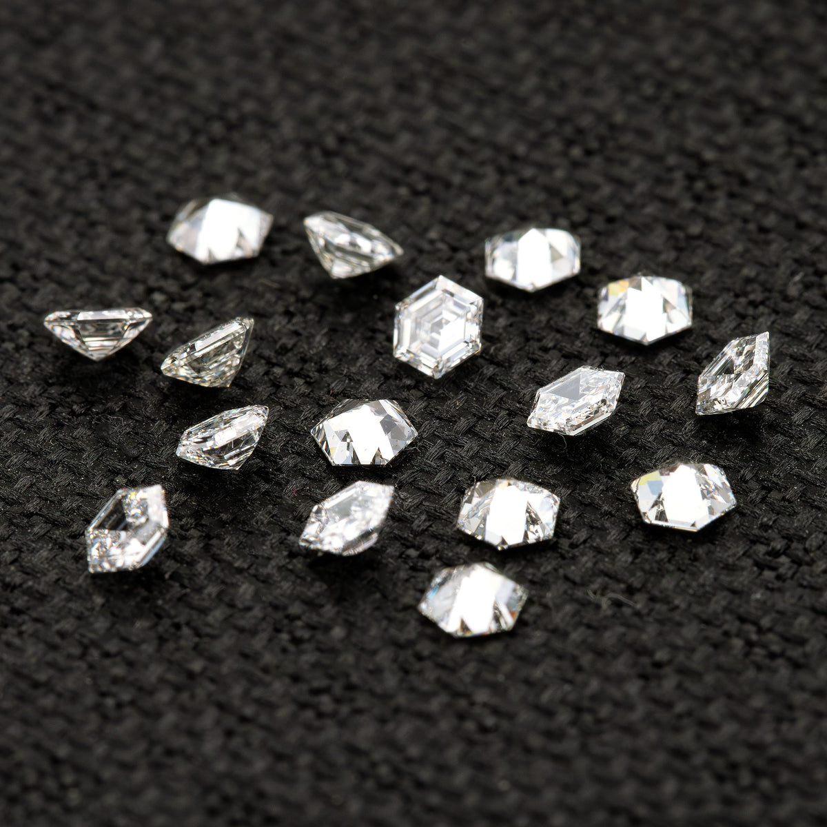 Scattered hexagonal diamonds on black fabric at different inclinations, showing side and reverse-facing views.