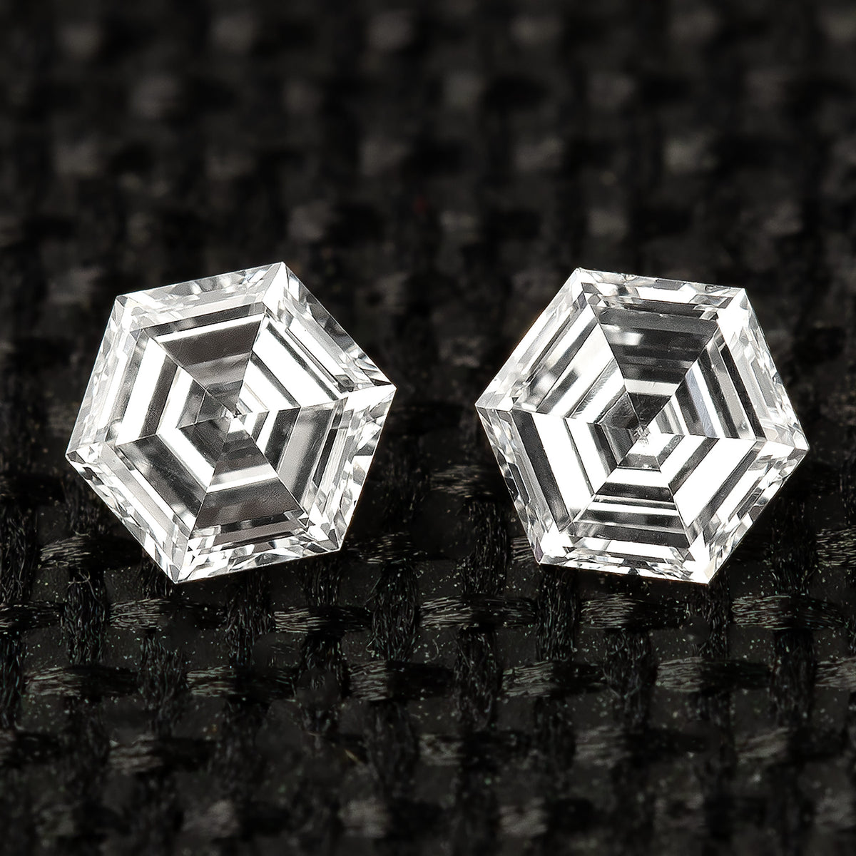 Two hexagonal diamonds side by side on black fabric, viewed face-up with contrasting step-facet reflections.