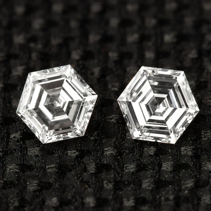 Two hexagonal diamonds side by side on black fabric, viewed face-up with contrasting step-facet reflections.