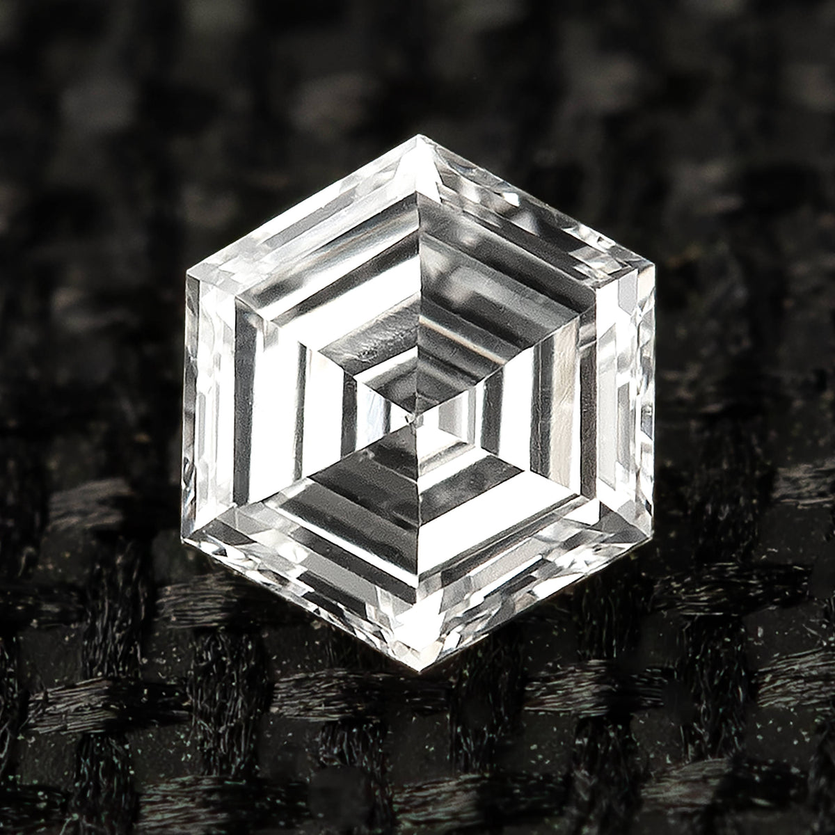 Macro face-up view of one hexagonal step-cut diamond resting on textured black fabric.