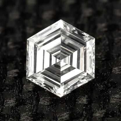 Macro face-up view of one hexagonal step-cut diamond resting on textured black fabric.