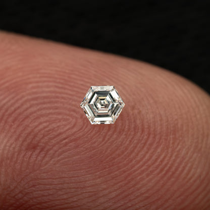 One hexagonal step-cut diamond resting face-up on a fingertip, giving realistic size context.