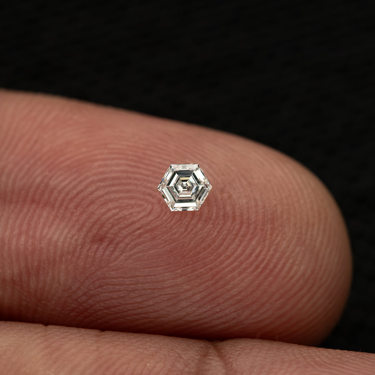 Wider fingertip view of a single small hexagonal diamond, showing its scale against fingerprint ridges.