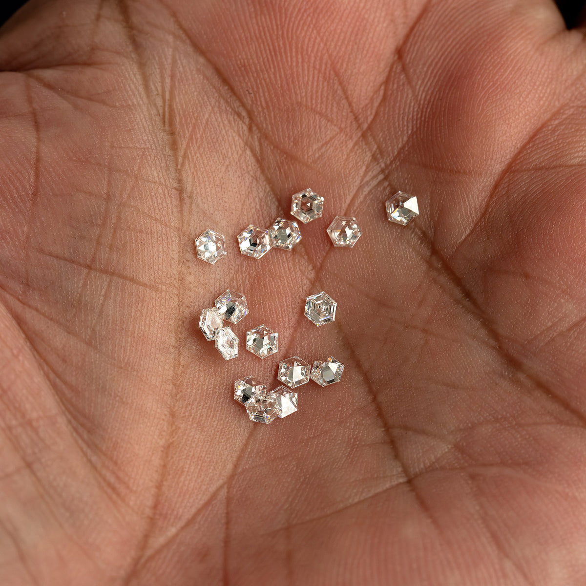 Loose hexagonal diamonds gathered in a palm, showing varied orientations and hand-scale context.
