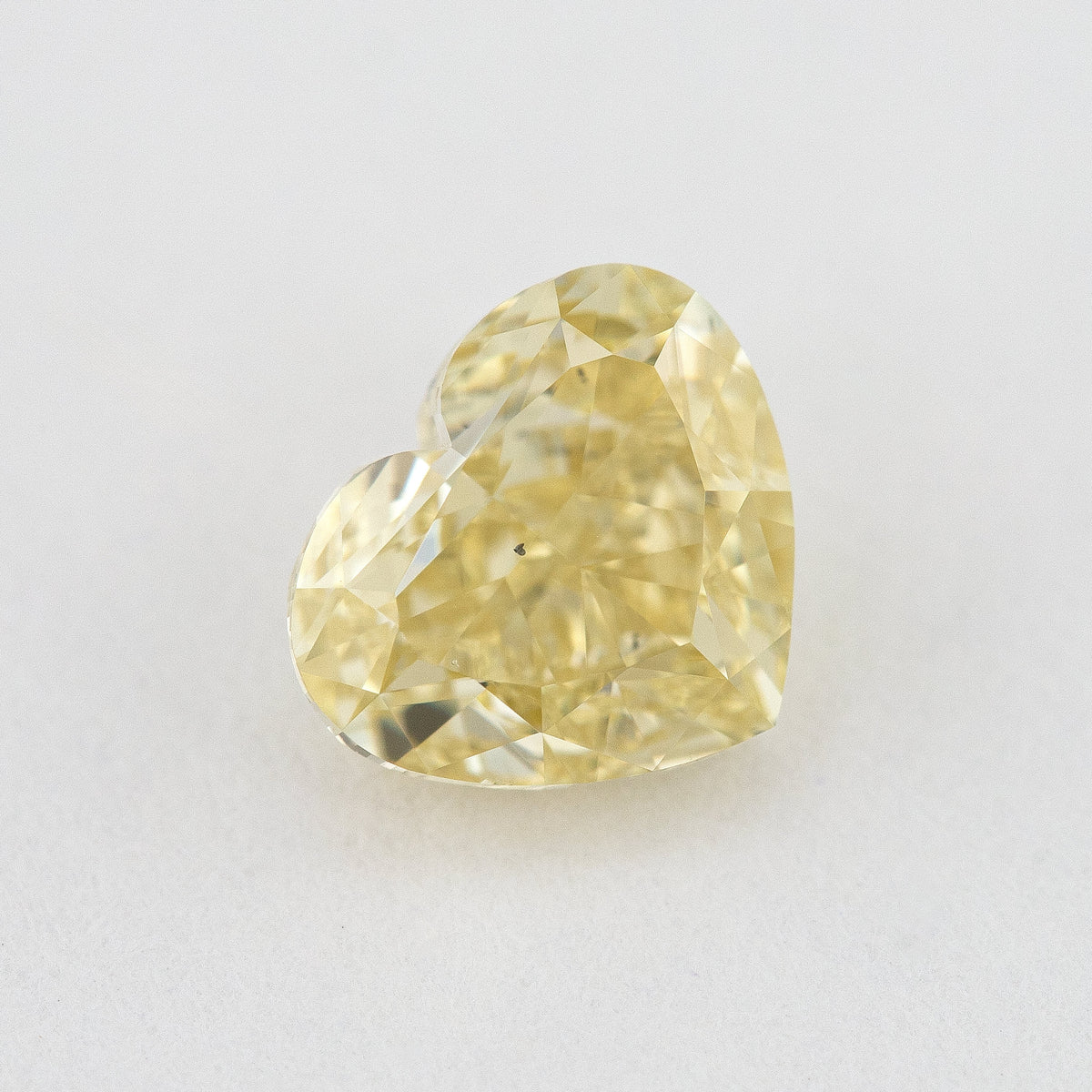 Face-up close-up of the yellow heart diamond on a pale background, showing its complete outline and crown facet reflections.