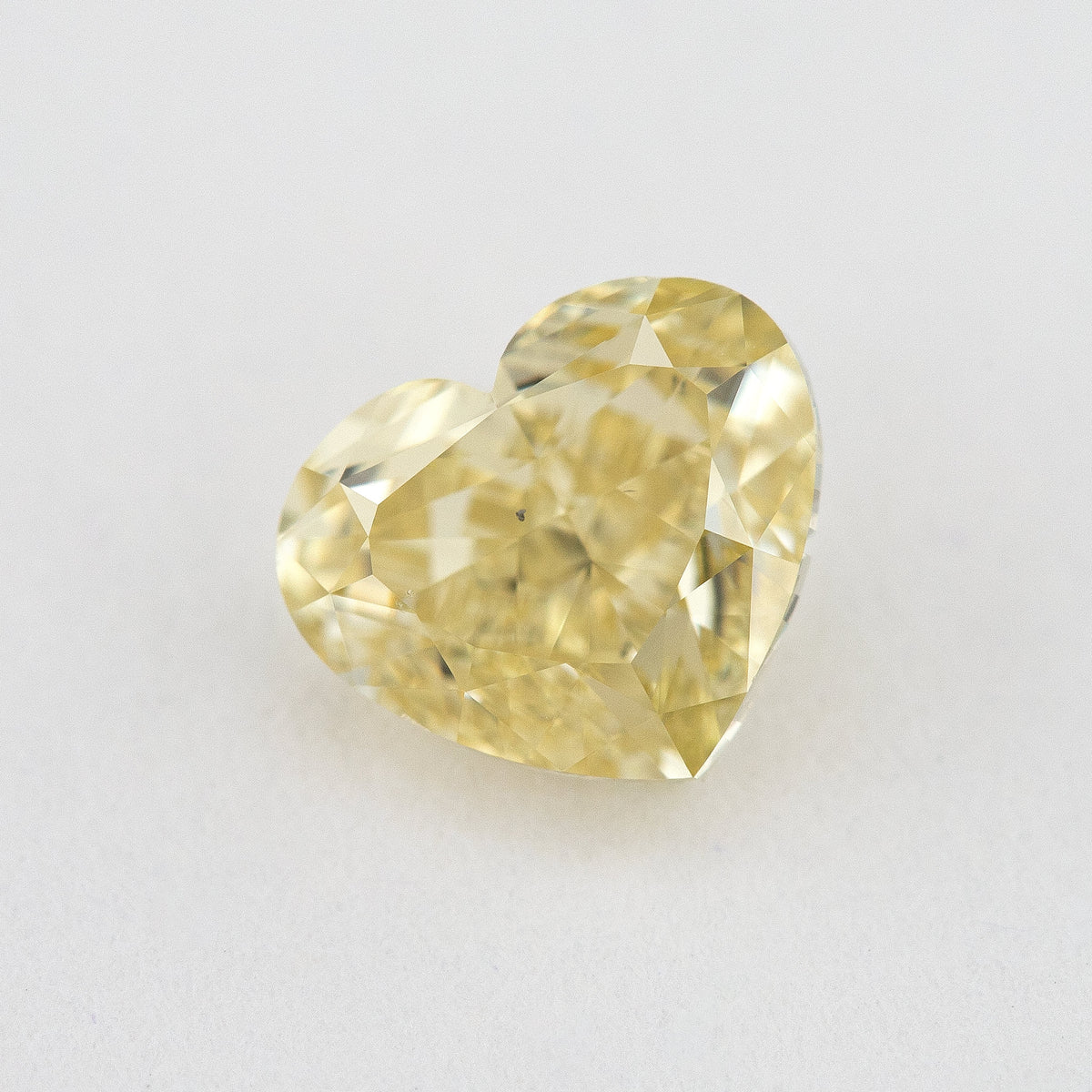 Alternate angled face-up view of the yellow heart diamond on a pale background, with a different pattern of light and dark facet reflections.