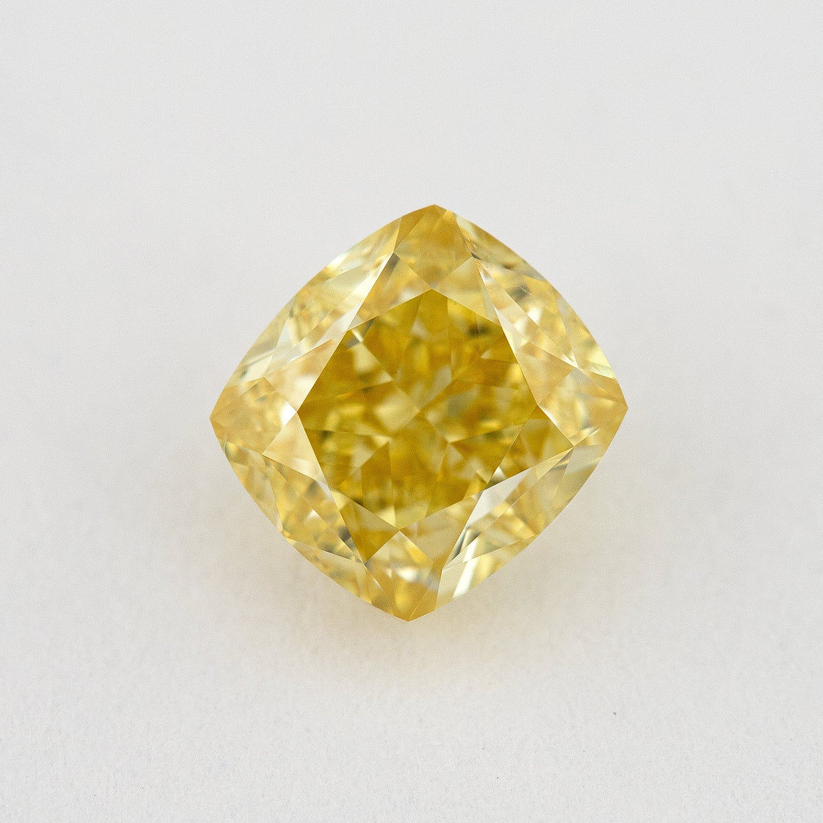 Face-up view of a yellow cushion-shaped natural diamond on a pale surface, showing its complete outline and crown facets.