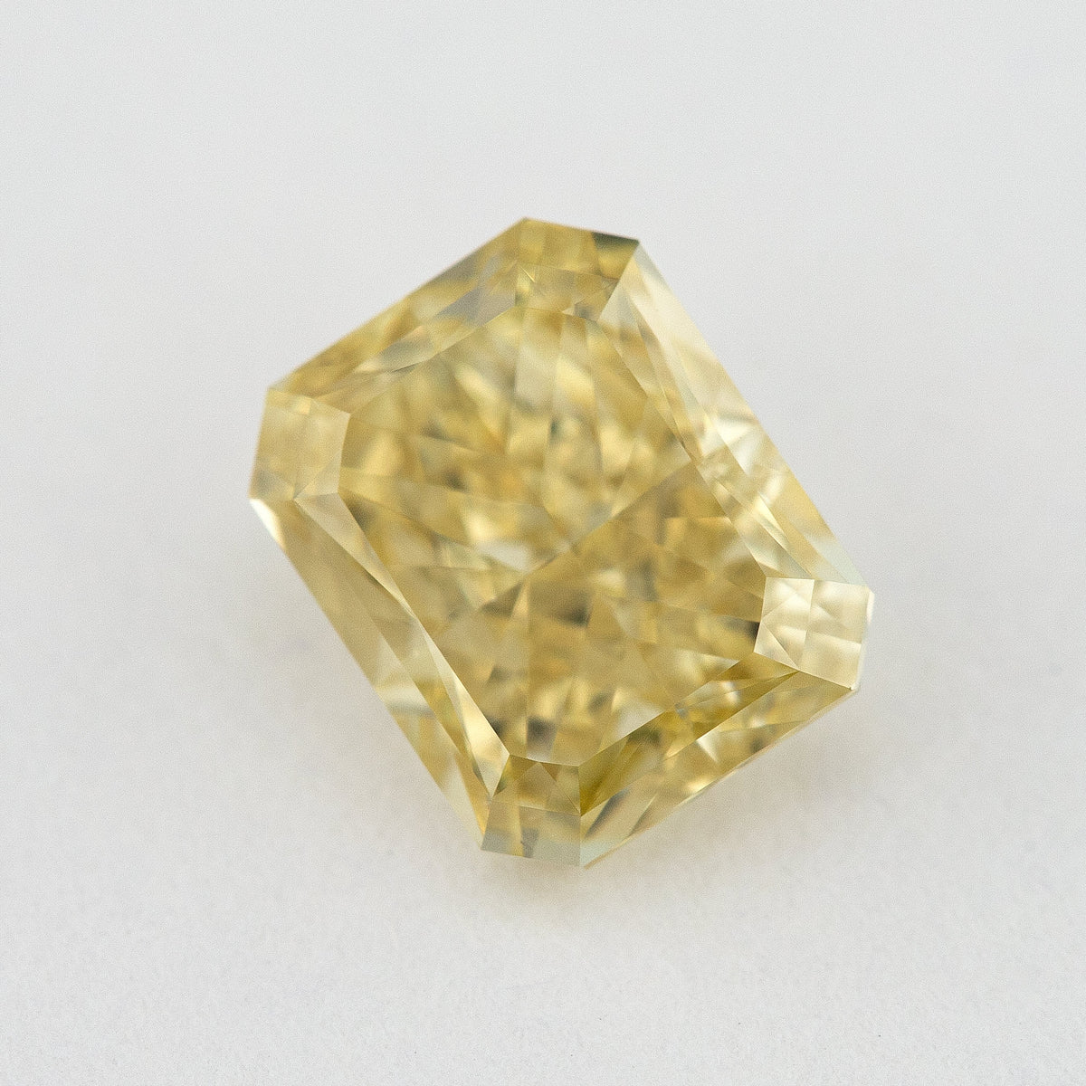Alternate angled face-up view of the yellow radiant diamond on a pale background, with a different pattern of light and dark facet reflections.