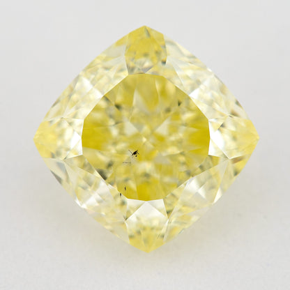 Yellow cushion-shaped natural diamond face-up on a pale surface, with dark internal characteristics visible near the center.