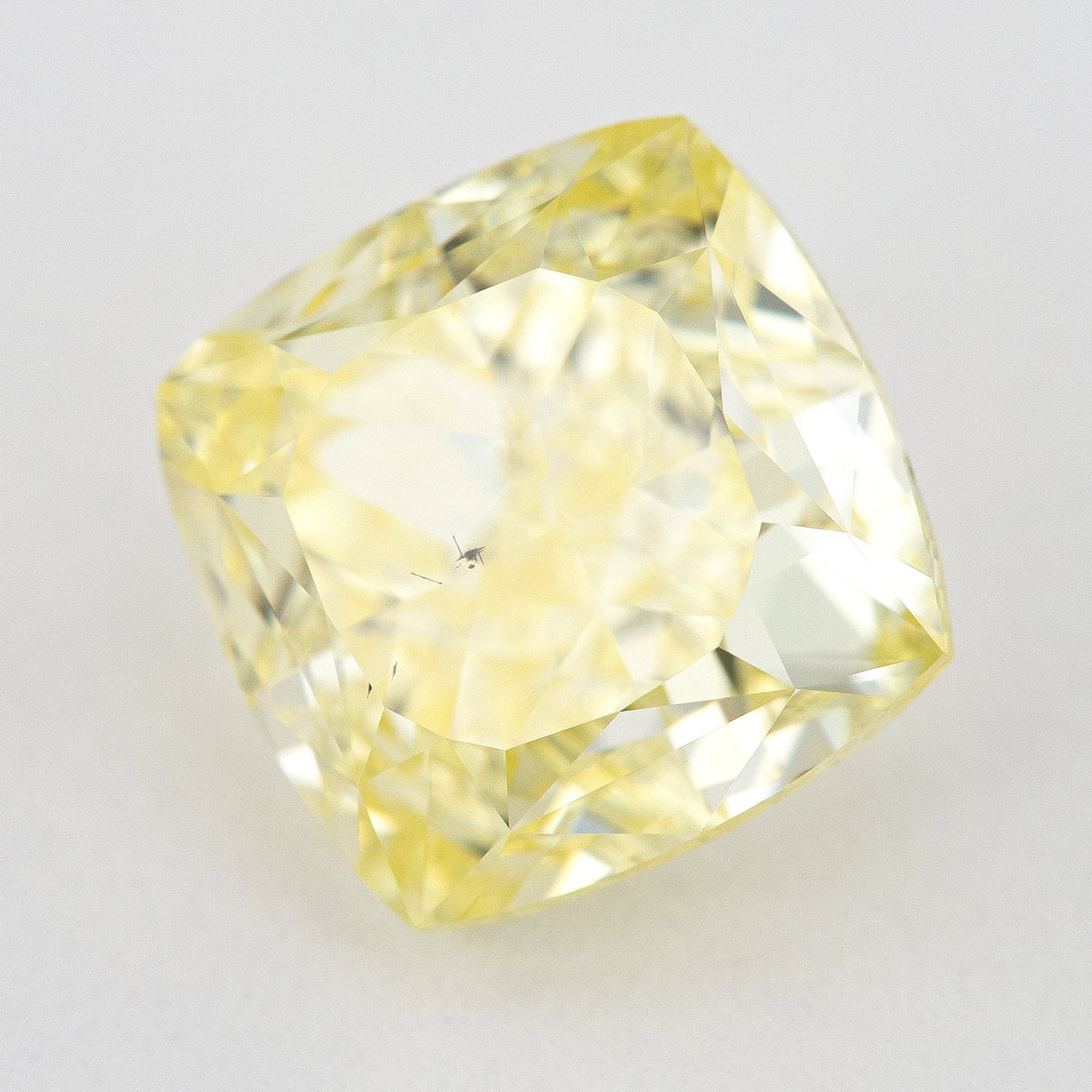Yellow cushion-shaped natural diamond tilted on a pale surface, showing its crown facets and complete outline.