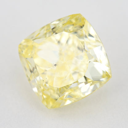 Yellow cushion-shaped natural diamond tilted on a pale surface, showing its crown facets and complete outline.