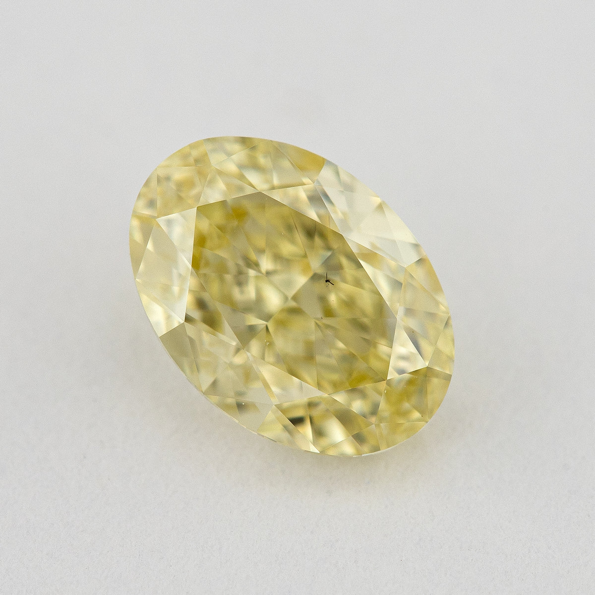 Face-up close-up of the yellow oval diamond on a pale background, showing its complete outline and crown facet reflections.